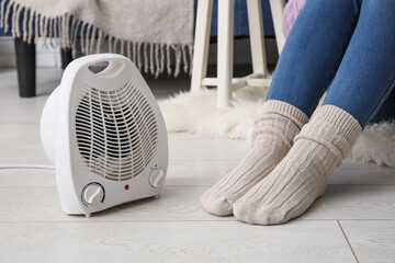Woman in warm socks near electric fan heater at home, closeup
