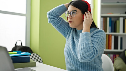 Fototapeta na wymiar Young hispanic woman student putting headphones on at library university