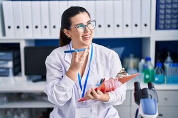 Young hispanic woman scientist talking on smartphone reading report at laboratory