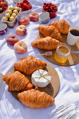Breakfast, picnic with croissants, cheese, honey and fruits on the white tablecloth
