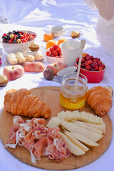 Breakfast, picnic with croissants, cheese, honey and fruits on the white tablecloth