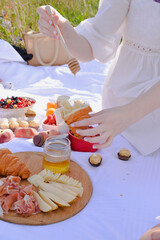women hand pouring honey to croissant on the picnic