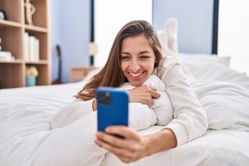 Young woman using smartphone lying on bed at bedroom