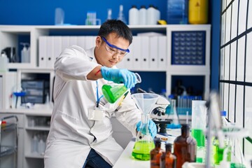 Young chinese man wearing scientist uniform measuring liquid at laboratory