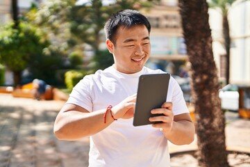 Fototapeta premium Young chinese man smiling confident using touchpad at park
