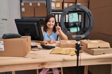 Hispanic girl with down syndrome working at small business ecommerce doing online tutorial surprised with an idea or question pointing finger with happy face, number one