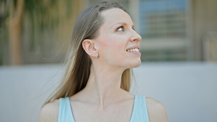 Young blonde woman smiling confident looking to the sky at street