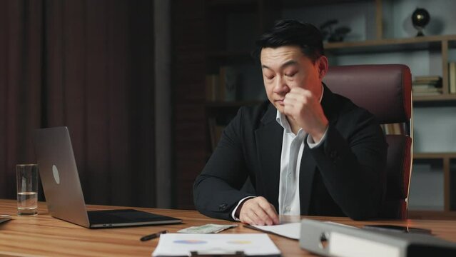 Anxious entrepreneur feeling upset due to lack of money. Pensive asian worker with sad face expression sitting in comfortable office chair and thinking how to get more cash.