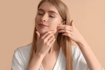 Young woman doing face building exercise on beige background, closeup