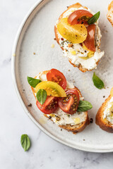 Bruschetta sandwiches with tomatoes, cream cheese, olive oil and basil on a plate on white marble background, top view, close up. Traditional italian antipasti