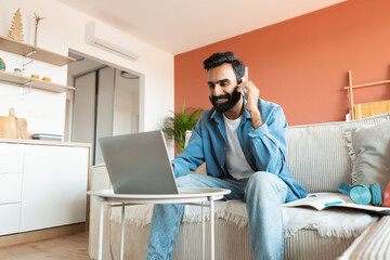 Arabic man talking on mobile phone while using laptop indoors