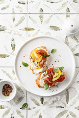 Bruschetta sandwiches with tomatoes, cream cheese, olive oil and basil on a plate on printed tile background, top view, copy space. Appetizer, italian antipasti