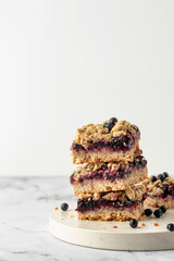 Stack of baked oatmeal squares with fresh blueberry on white tray on marble background with text space