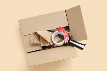 Packing tape dispenser and cardboard box on beige background