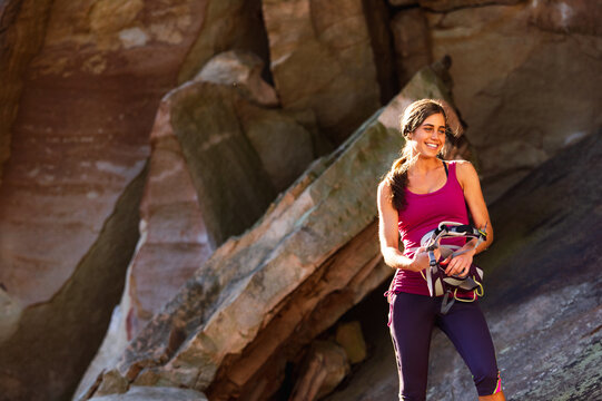An athletic young woman in a pink tank top holds rock climbing gear while standing in front of a sandstone cliff in Tennessee