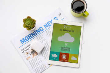 Tablet computer with weather forecast, earphones, newspaper and coffee cup on white background