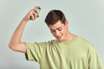 Young handsome smiling guy applies therapeutic hair mousse or lotion using atomizer. Brown-haired...