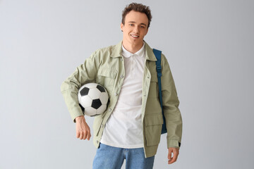 Male student with backpack and soccer ball on grey background