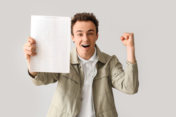 Happy male student with answer sheet for school test on grey background