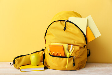 Yellow school backpack with notebooks, apple and scissors on wooden table near wall