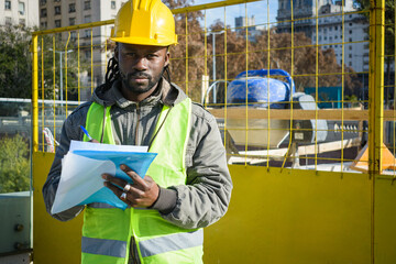 black male engineer at a construction site outdoors with holding a folder looking at the camera.