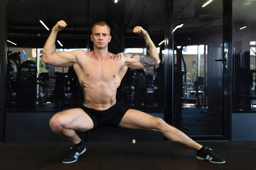 Fototapeta na wymiar young athlete man go in for sport in fitness club, show his muscles. European guy on workout in gym