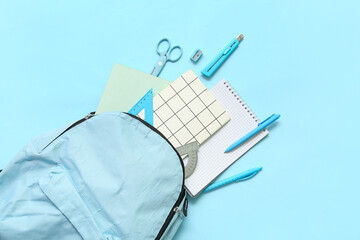 School backpack with different stationery on blue background