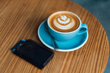 Blue mug cappuccino and coffee art with wallet and credit card lying on a wooden table. Top view. 