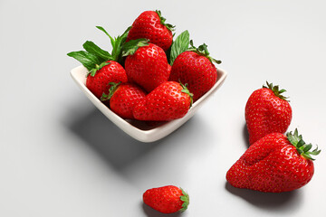 Bowl with fresh strawberries and mint on grey background