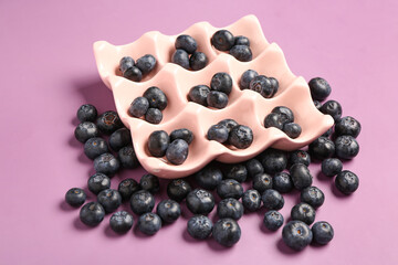 Ice cube tray with fresh blueberries on lilac background
