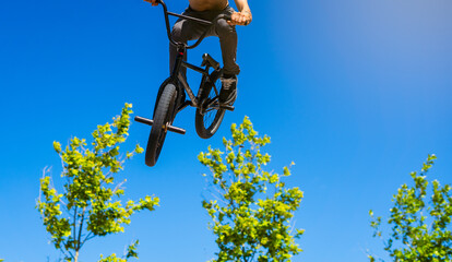 bmx rider shirtless with black bike jumping on a blue sky