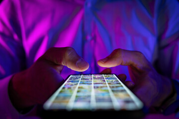 man scrolling mobile phone screen in dark room with neon lights. internet browsing, social media and marketing
