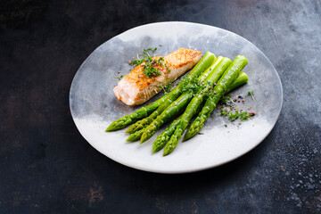 Traditional glazed green asparagus with salmon fillet and herbs served as close-up on a design plate with copy space