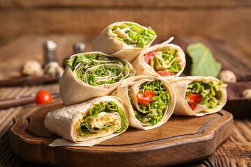 Board of tasty lavash rolls with vegetables and greens on wooden background