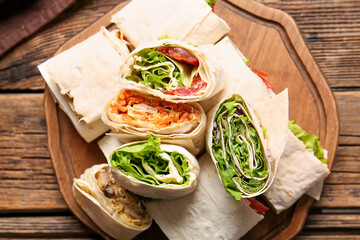 Board of tasty lavash rolls with vegetables and greens on wooden background