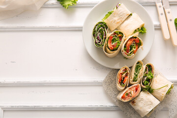 Plate and board of tasty lavash rolls with vegetables on white wooden background