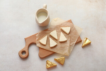 Board with triangles of tasty processed cheese and milk on light background
