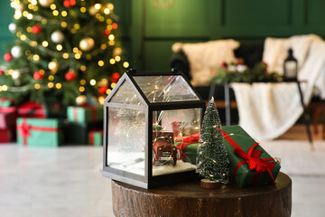Decorative lantern with Christmas tree and gift boxes on table in living room