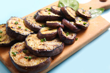Board with delicious grilled eggplants on light blue background, closeup