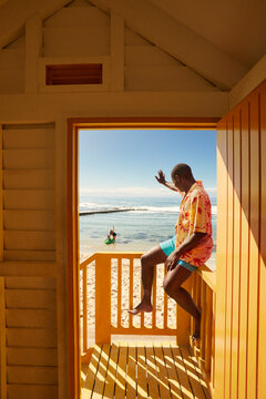 Young father waving at family from beach side cabana in Cape Town
