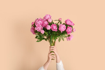 Female hands with bouquet of pink peonies on beige background