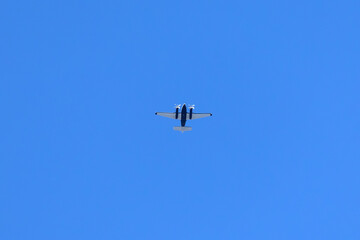 A twin-engine plane flying in a blue sky between clouds. Transportation.