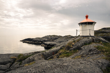 un petit phare sur des rochers au bord d'une mer calme 