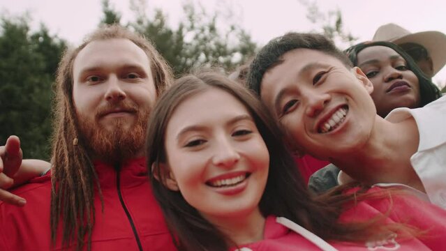 Young girl shooting a funny selfie video with her multiracial friends when they are smiling and looking at the camera outdoors at the picnic. Concept of a cheerful summer party