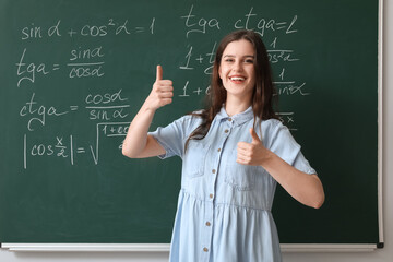 Female Math teacher showing thumbs-up near chalkboard in classroom