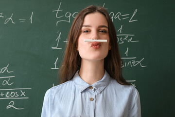 Female Math teacher with chalk near chalkboard in classroom, closeup