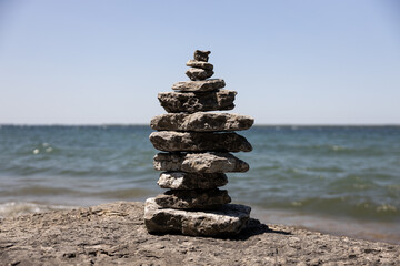 Fototapeta na wymiar simple stack of stones on a beach in Lake Ontario New York on a summer afternoon with blue skies on a blurry background, cairns