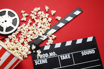 Bucket with tasty popcorn, clapperboard and film reel on red background