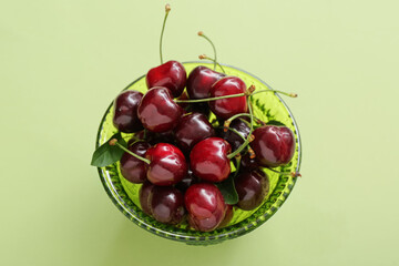 Bowl with sweet cherries on green background