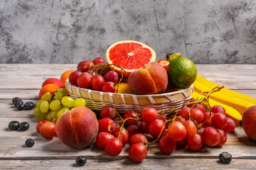 Wicker bowl with different fresh fruits on grey wooden background